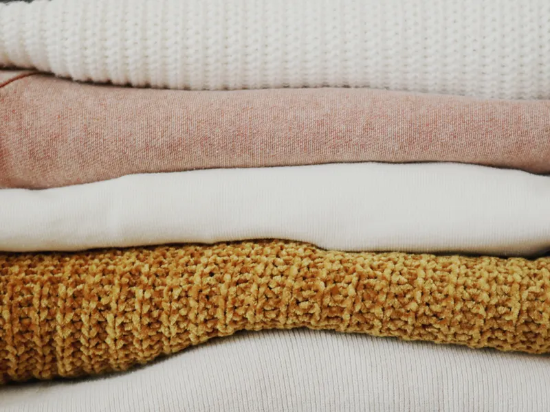Folded blankets and knitwear stacked in soft colours