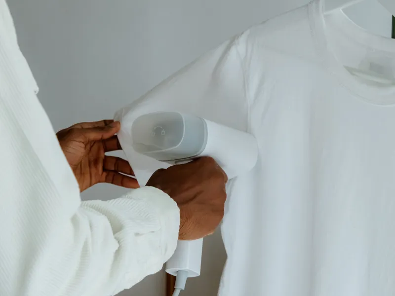 Hands steam-ironing a white shirt on a hanger